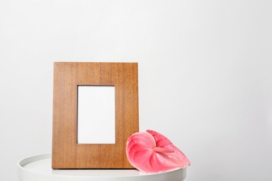 Photo of Blank frame and flower on table against white background. Mock up for design