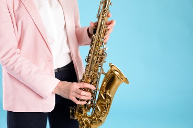 Photo of Woman with saxophone on light blue background, closeup. Space for text