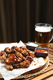 Tasty chicken wings, sauces and mug of beer on wooden table, space for text. Delicious snack