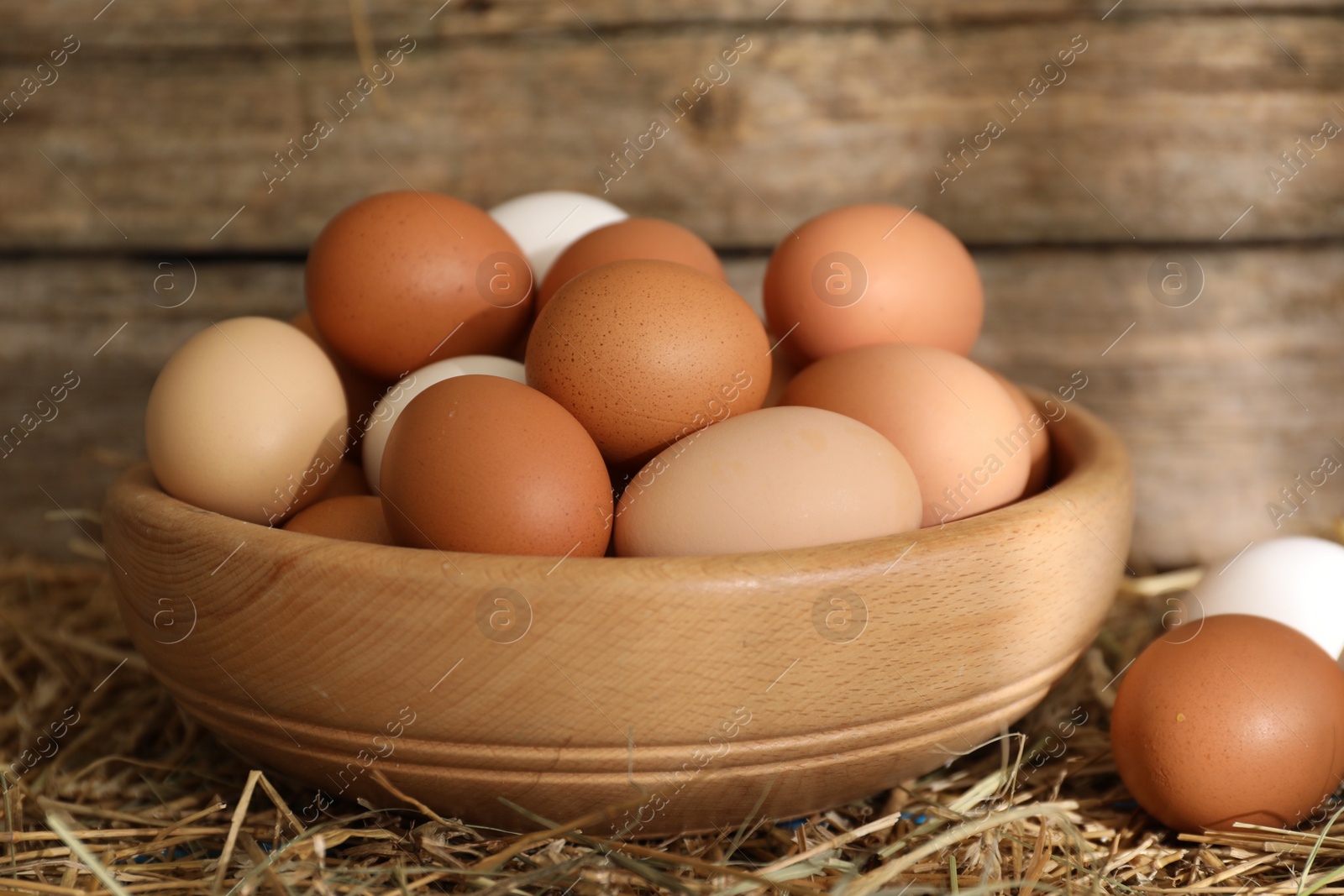 Photo of Fresh chicken eggs in bowl on dried straw, closeup