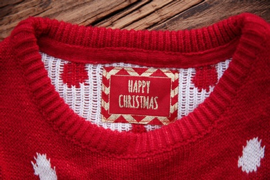 Christmas sweater with tag on wooden background, closeup