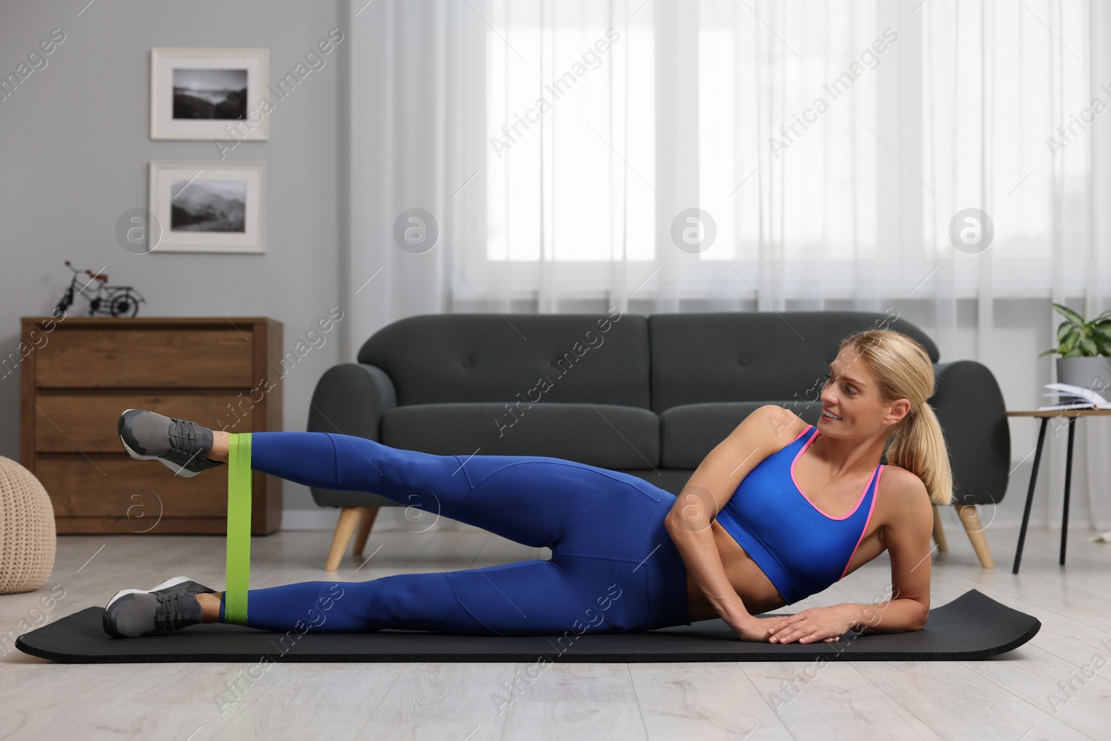 Photo of Athletic woman doing exercise with fitness elastic band on mat at home