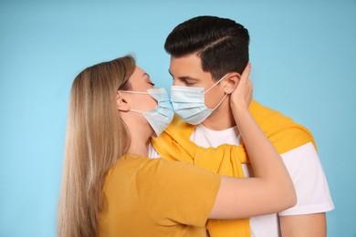 Photo of Couple in medical masks trying to kiss on light blue background