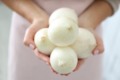Photo of Woman holding white onions on blurred background, closeup