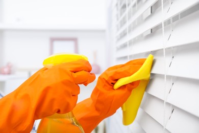 Woman cleaning window blinds with detergent and rag indoors, closeup