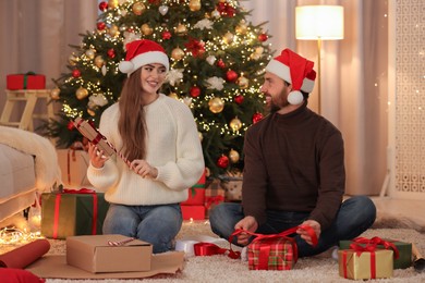 Photo of Happy couple in Santa hats decorating Christmas gift at home