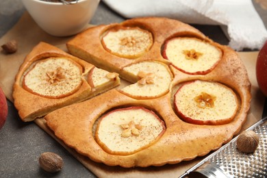 Photo of Tasty apple pie, nutmeg seeds and grater on grey table