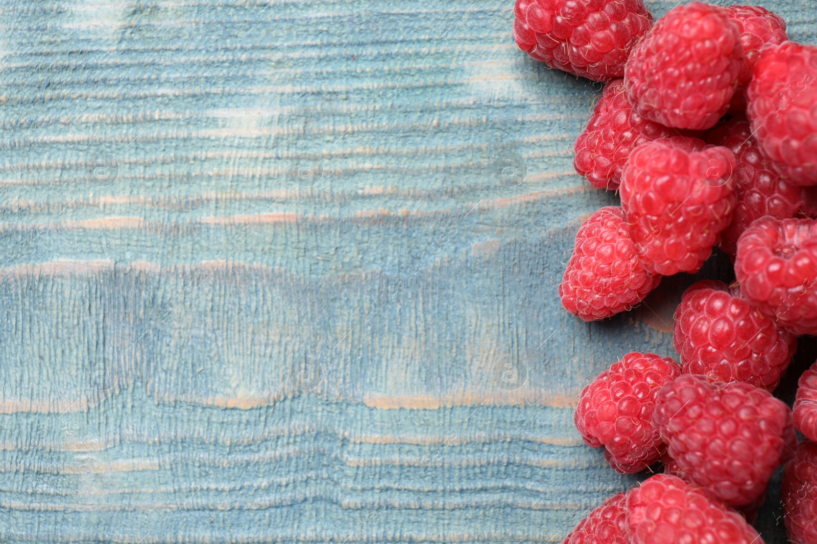 Photo of Delicious fresh ripe raspberries on blue wooden table, top view. Space for text