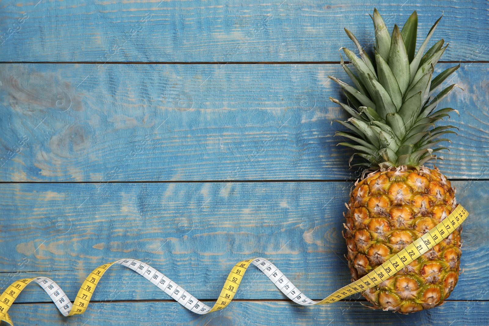 Photo of Flat lay composition with pineapple, measuring tape and space for text on wooden background. Weight loss concept