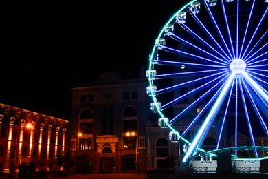 Photo of Beautiful glowing Ferris wheel on city street at night