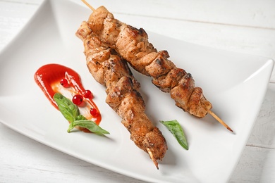 Plate with juicy shish kebab and sauce on table, closeup