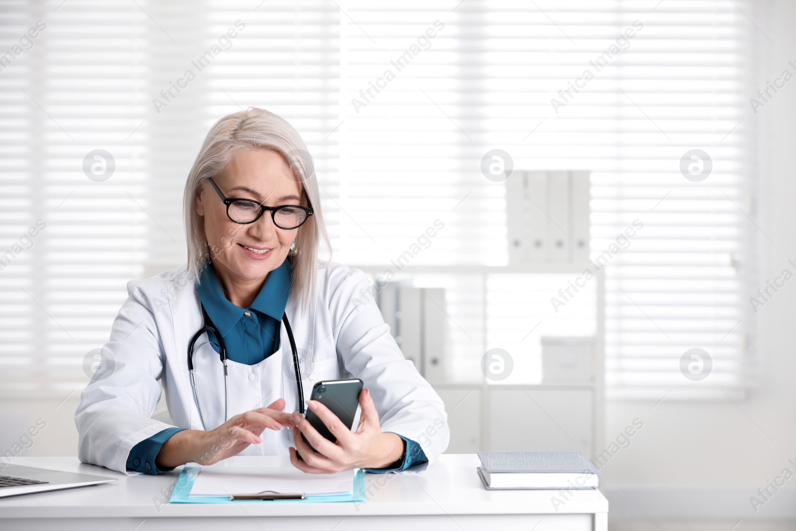 Photo of Mature female doctor with smartphone at table in office