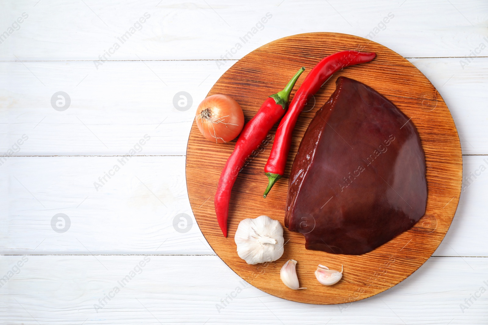 Photo of Piece of raw beef liver with chili peppers, onion and garlic on white wooden table, top view. Space for text