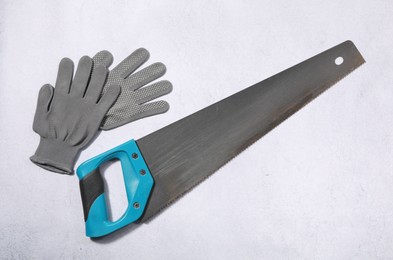 Photo of Saw with light blue handle and gloves on gray background, flat lay