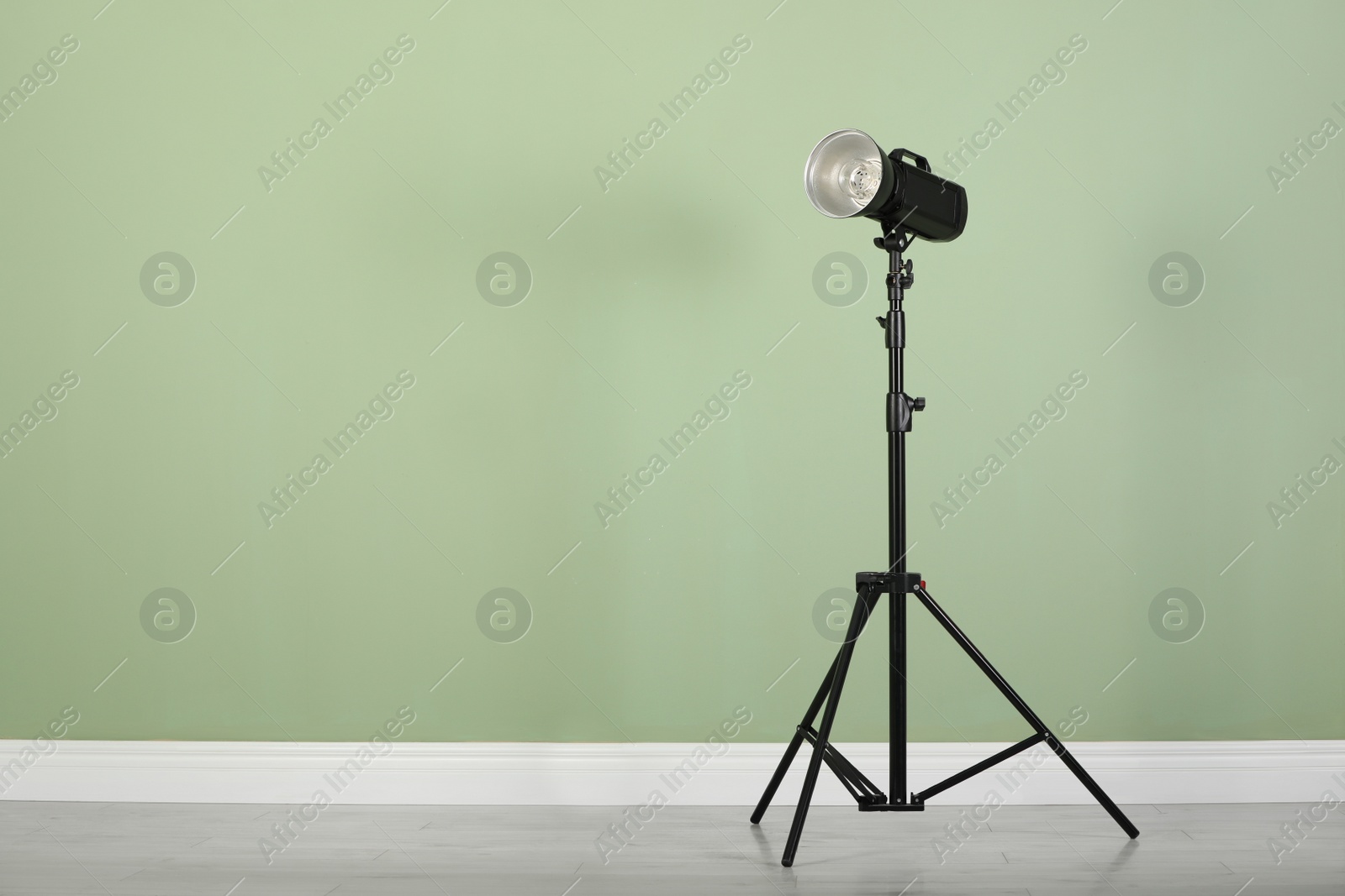 Photo of Studio flash light with reflector on tripod near pale green wall in room, space for text. Professional photographer's equipment