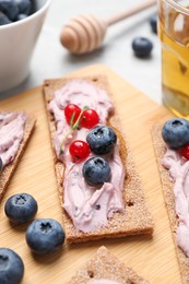 Tasty cracker sandwiches with cream cheese, blueberries, red currants, thyme and honey on wooden board, closeup