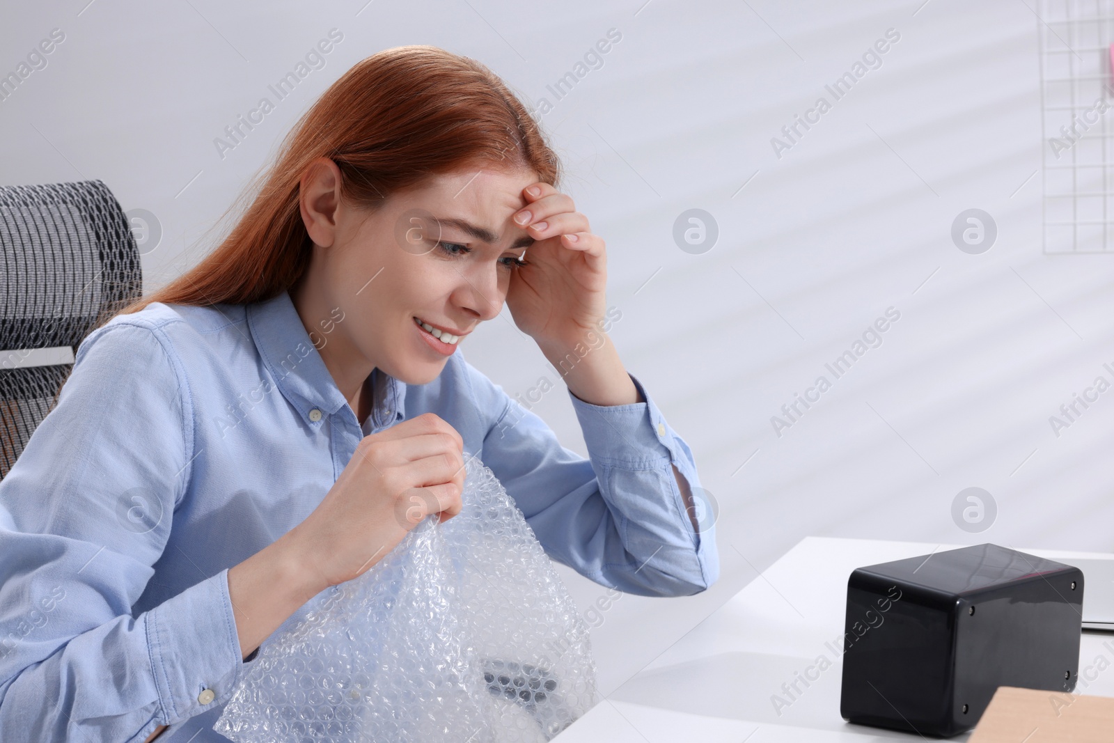 Photo of Emotional woman popping bubble wrap at desk in office. Stress relief