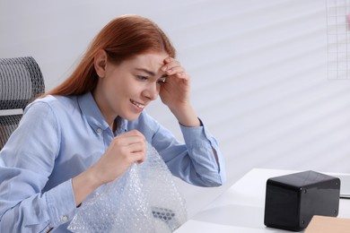 Emotional woman popping bubble wrap at desk in office. Stress relief