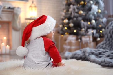 Little baby wearing Santa hat on floor at home. First Christmas