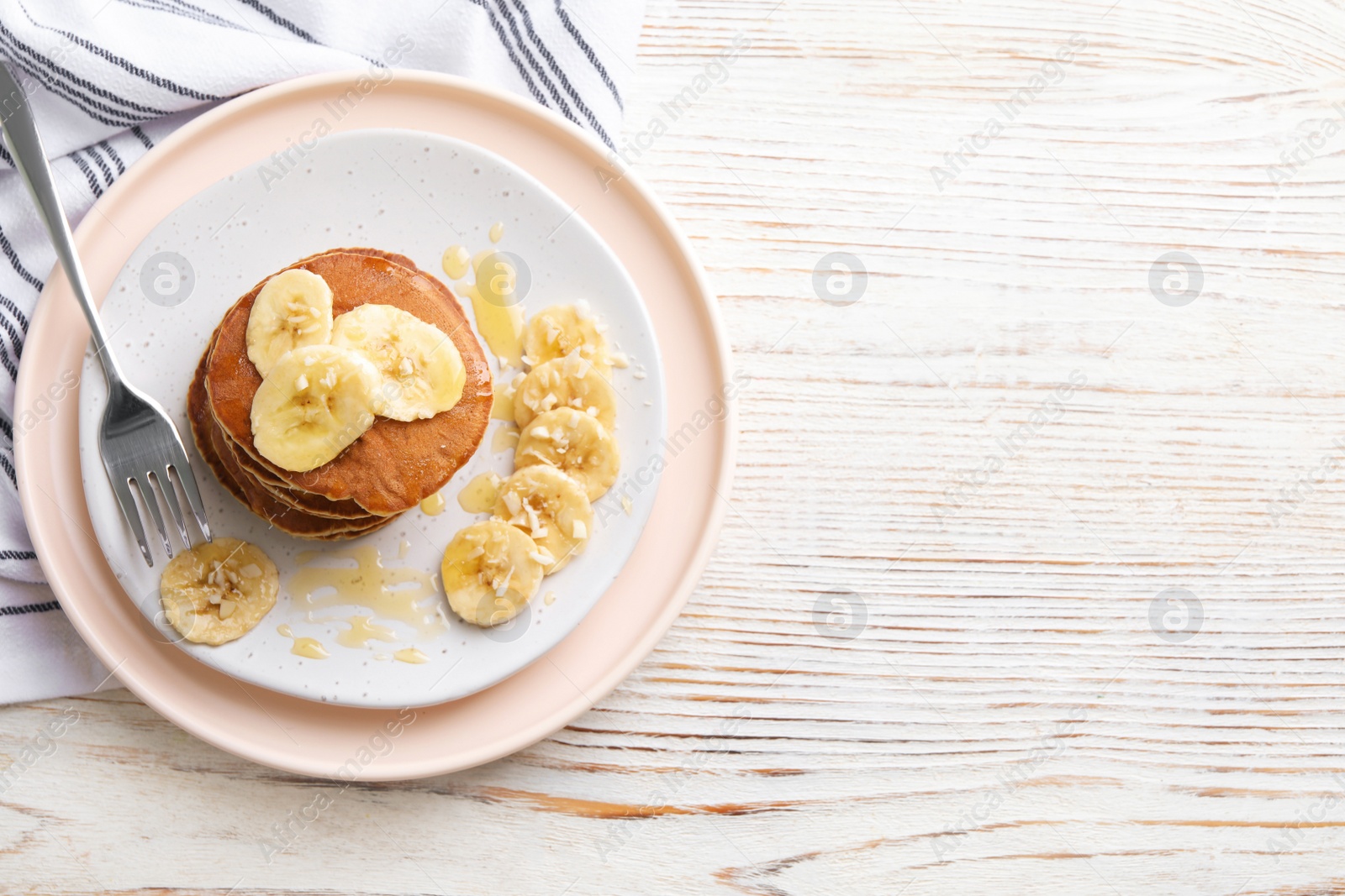 Photo of Plate of banana pancakes with honey served on white wooden table, top view. Space for text