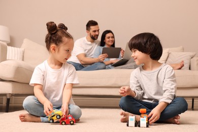 Photo of Cute children playing with toys while parents using gadgets on sofa in living room