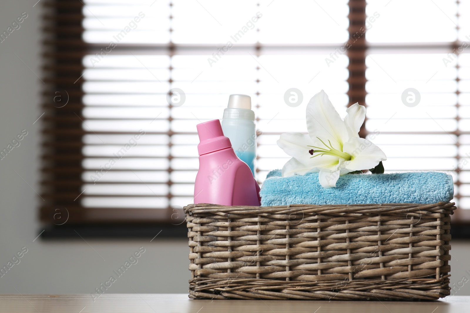 Photo of Clean towels with lily and detergents in basket on table indoors. Space for text