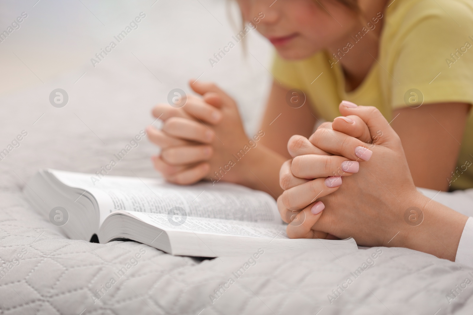 Photo of Girl and her godparent praying over Bible together indoors, closeup. Space for text