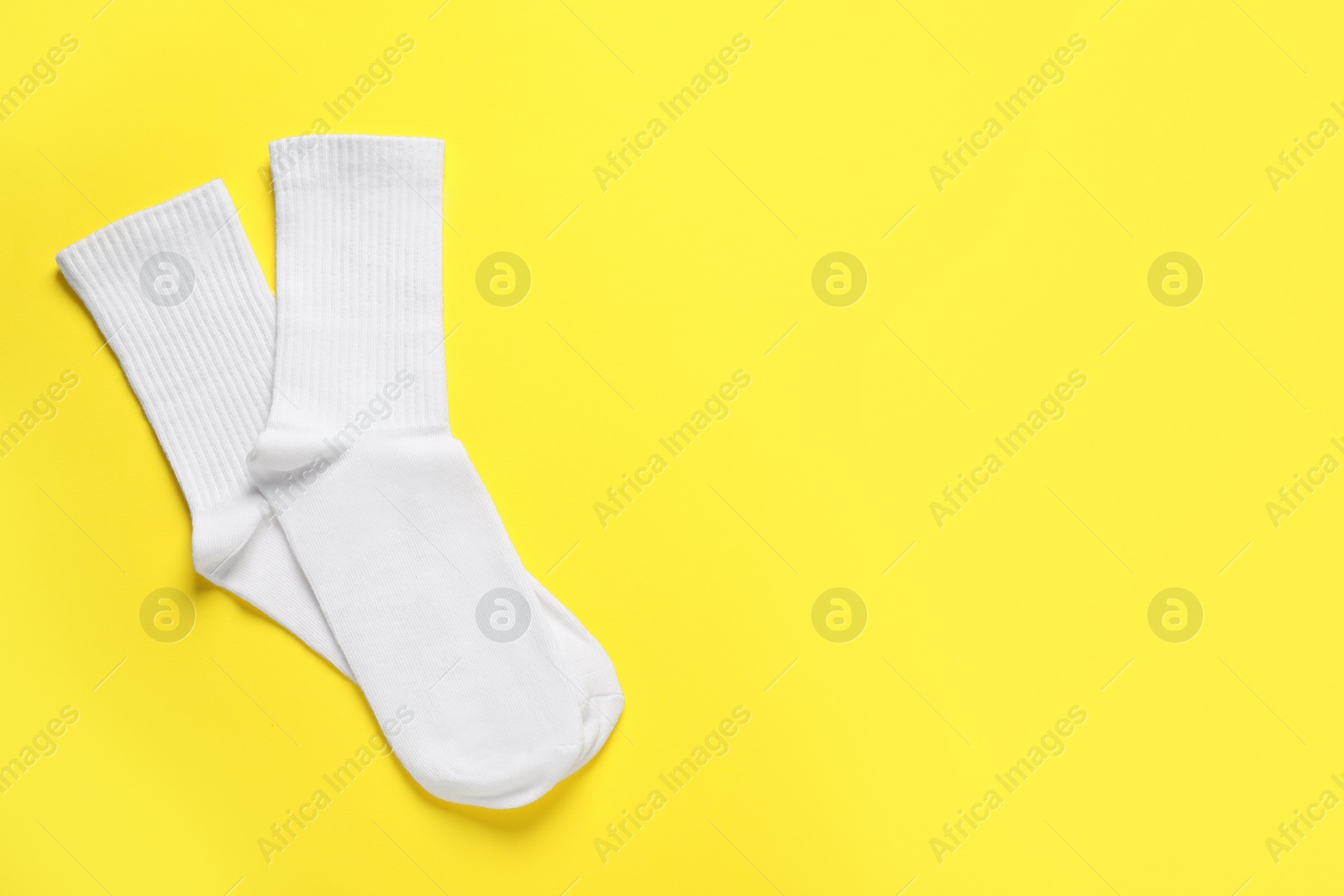 Photo of Pair of white socks on yellow background, flat lay. Space for text