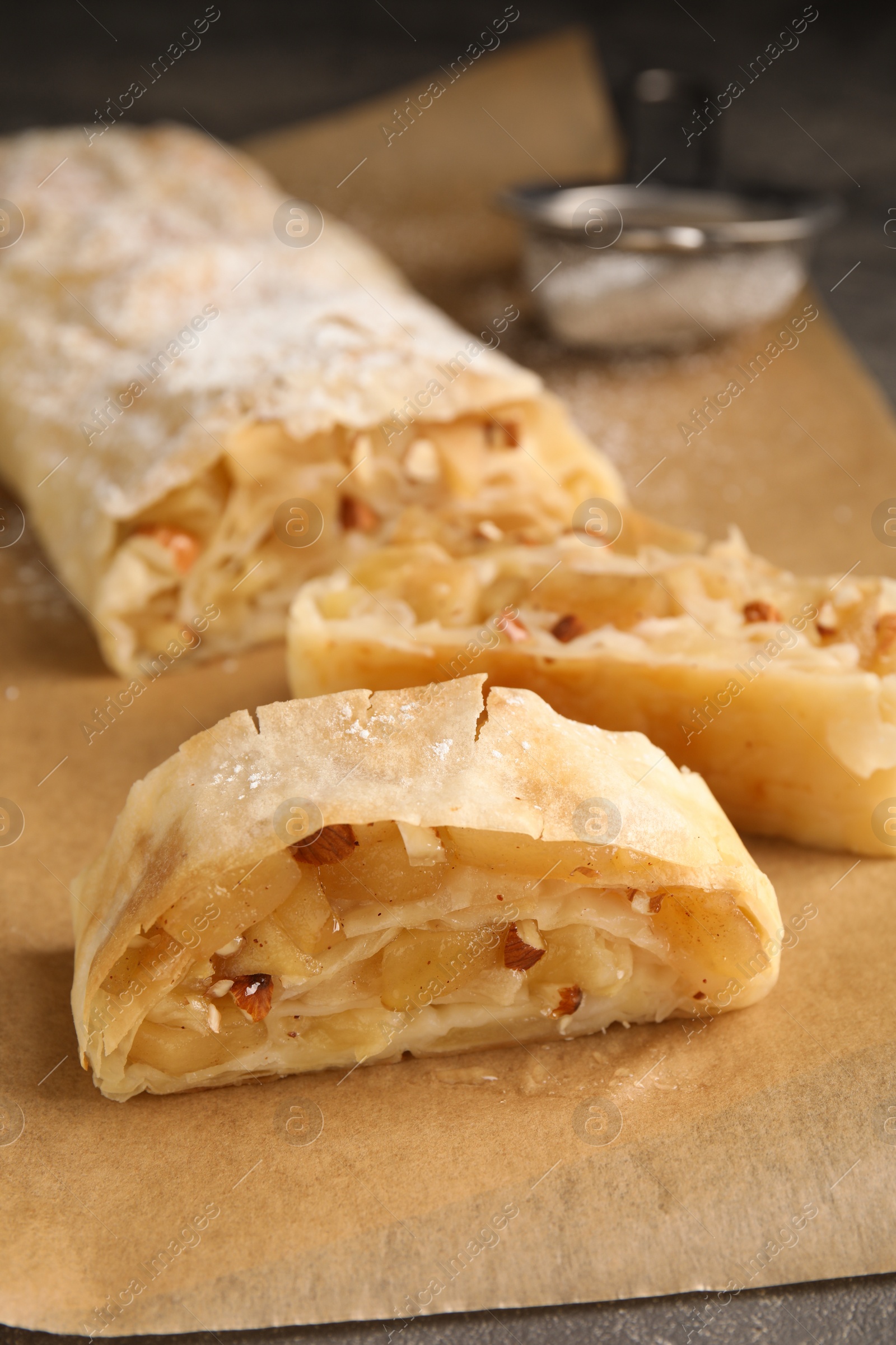 Photo of Delicious apple strudel with almonds on parchment, closeup