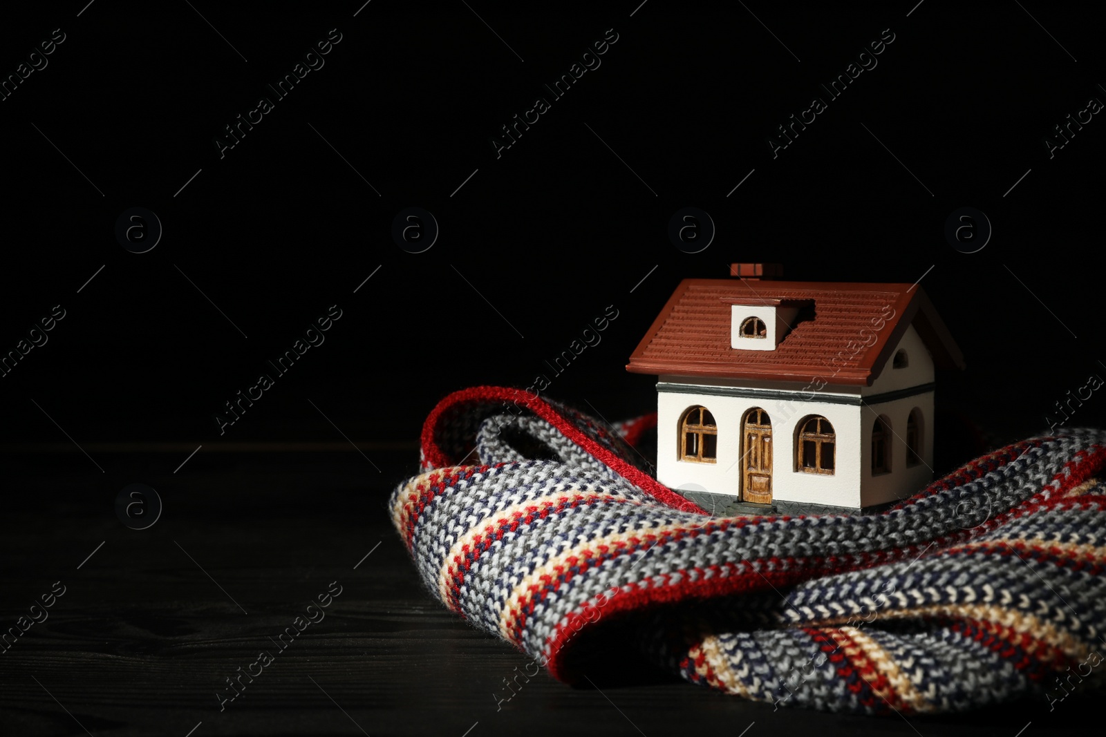 Photo of House model and scarf on table against black background, space for text. Heating efficiency