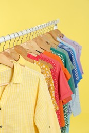 Photo of Bright clothes hanging on rack against yellow background. Rainbow colors