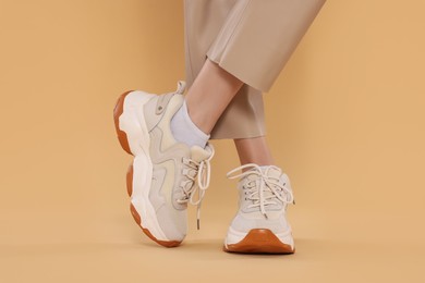 Woman wearing pair of new stylish sneakers on beige background, closeup