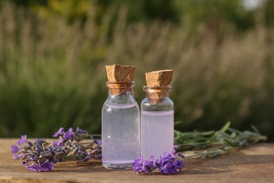 Bottles of natural lavender essential oil and flowers on wooden table outdoors