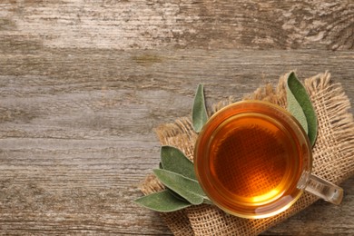 Photo of Cup of aromatic sage tea and fresh leaves on wooden table, top view. Space for text