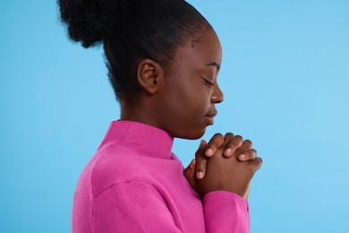 Woman with clasped hands praying to God on light blue background