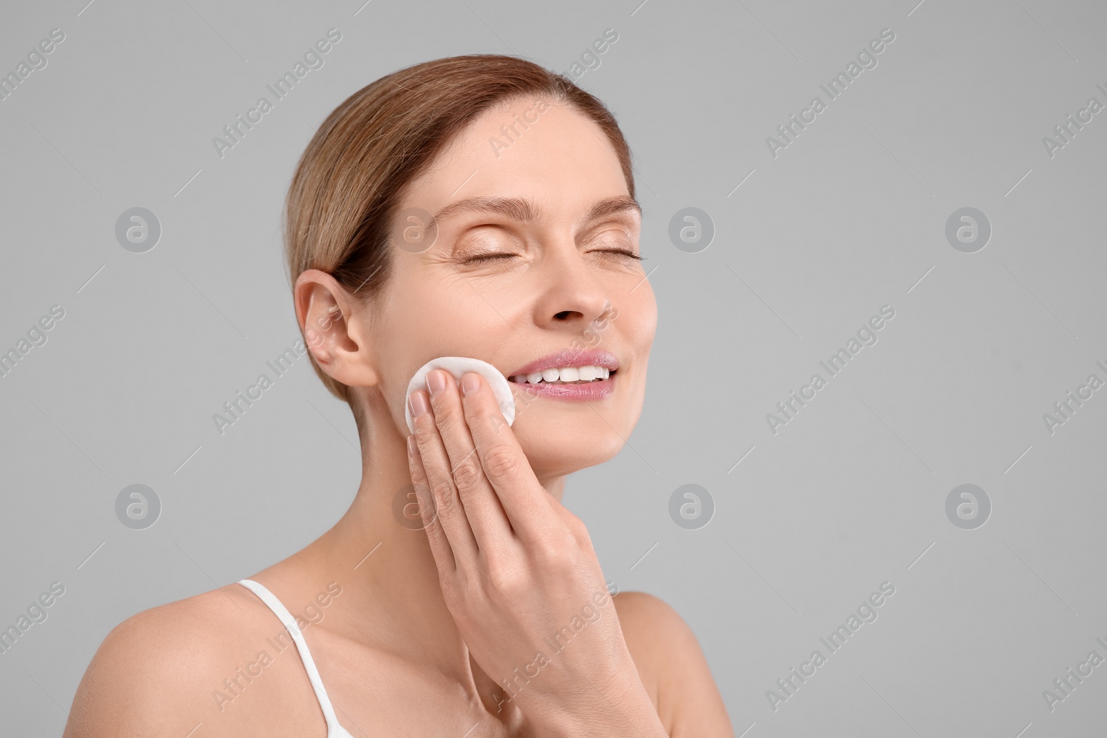 Photo of Beautiful woman removing makeup with cotton pad on gray background, space for text