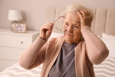 Senior woman with headache in bedroom at home