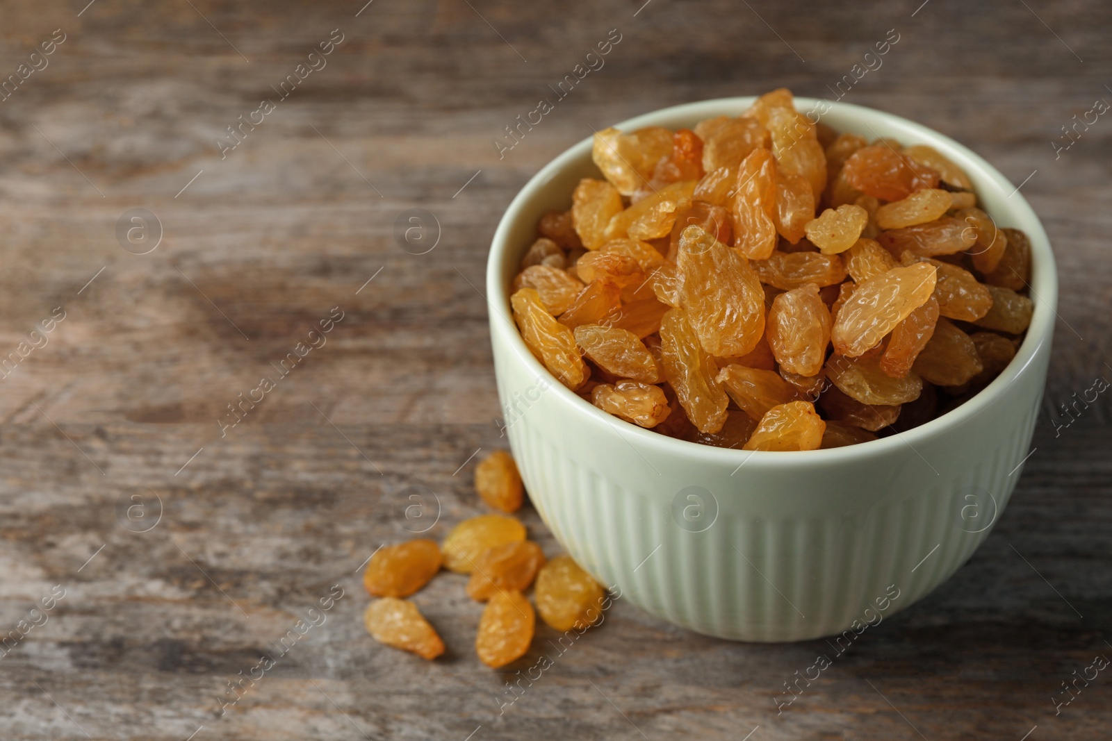 Photo of Bowl with raisins and space for text on wooden background. Dried fruit as healthy snack