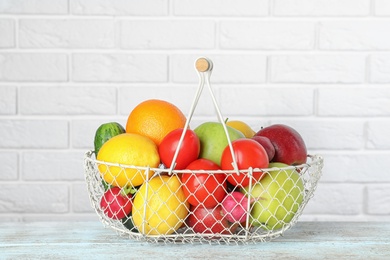 Photo of Basket with ripe fruits and vegetables on table against white brick wall