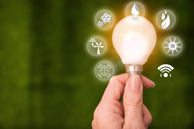 Image of Energy efficiency concept. Woman holding light bulb surrounded by icons, closeup