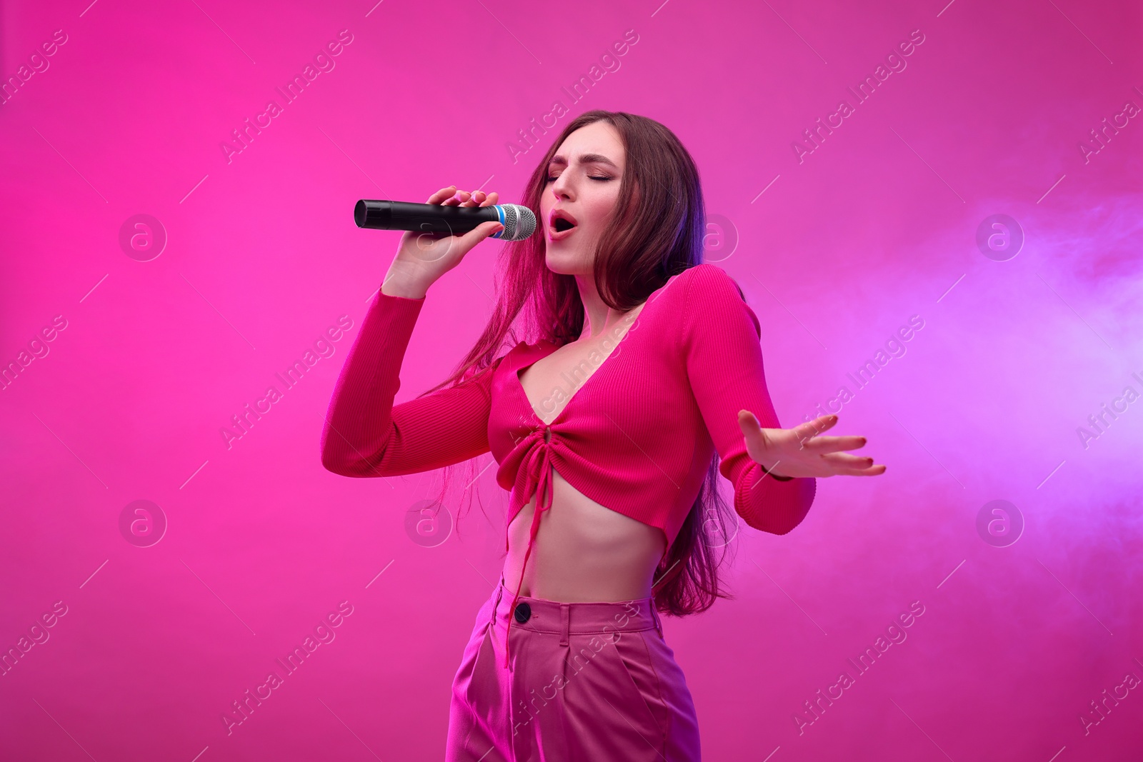 Photo of Beautiful woman with microphone singing on pink background