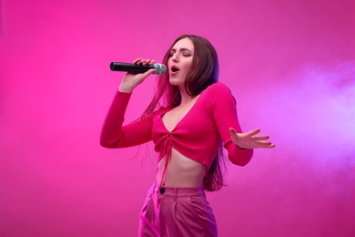 Beautiful woman with microphone singing on pink background