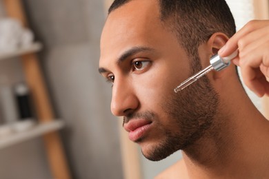 Photo of Handsome man applying cosmetic serum onto face in bathroom, closeup. Space for text
