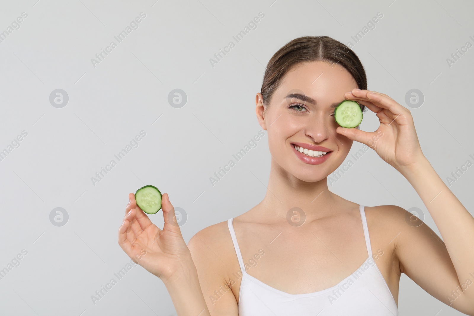 Photo of Young woman with cucumber slices on white background, space for text. Eye skin care