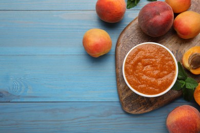 Photo of Apricot puree in bowl and fresh fruits on light blue wooden table, flat lay. Space for text