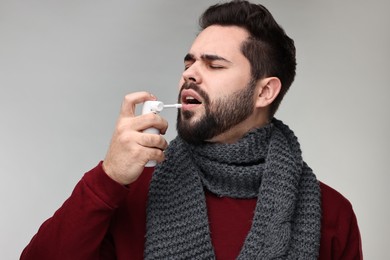 Photo of Young man with scarf using throat spray on grey background