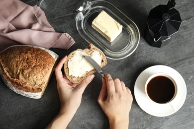 Photo of Woman spreading tasty butter onto bread over dark table, top view