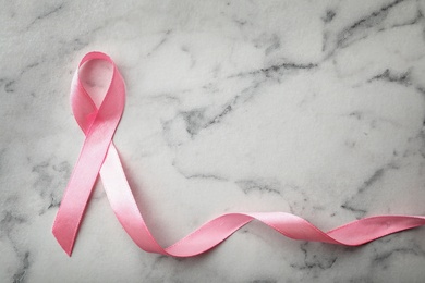 Photo of Pink ribbon on marble background, top view with space for text. Breast cancer awareness concept