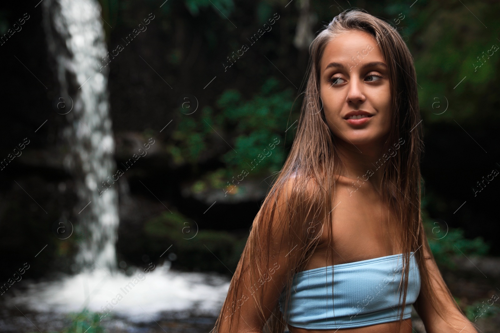 Photo of Beautiful young woman in light blue bikini relaxing near mountain waterfall. Space for text