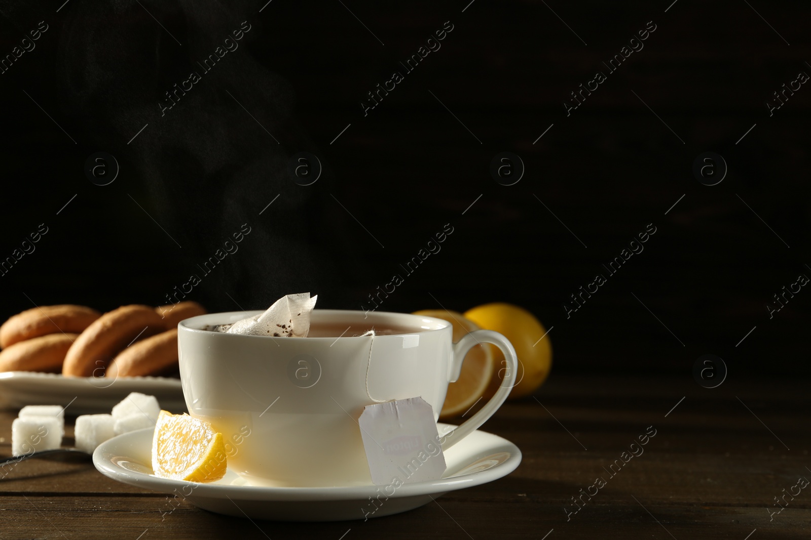 Photo of Tea bag in ceramic cup of hot water and lemon on dark wooden table. Space for text